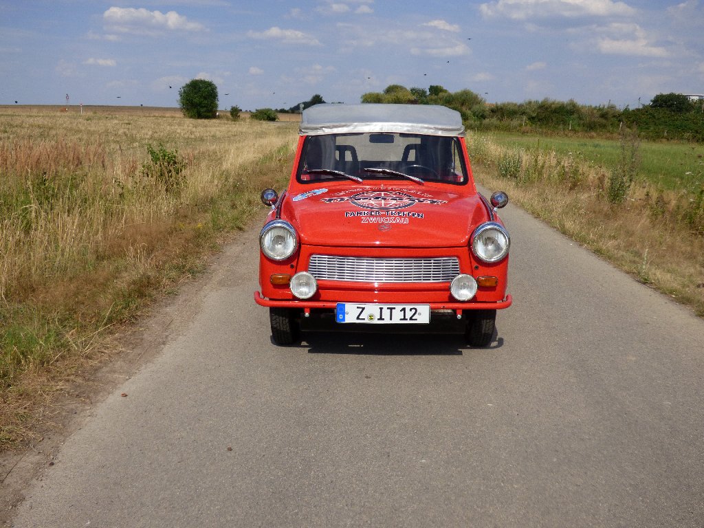 Frontansicht des Inter Trab Forstkübel "Super Trabi" mit geschlossenem Verdeck auf einer Straße zwischen Feldern und Wiesen.